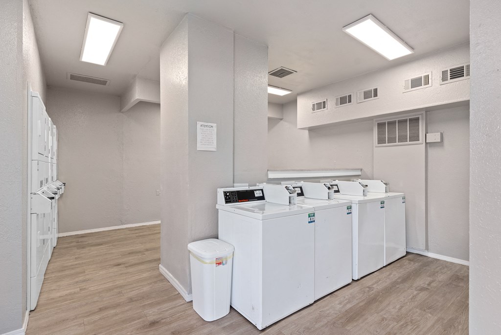 a community laundry room with four washers and dryers and a row of sinks