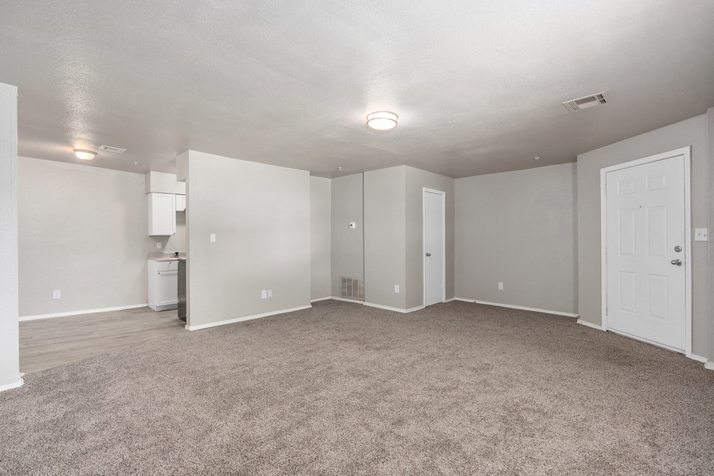 an empty living room with carpet and a white kitchen