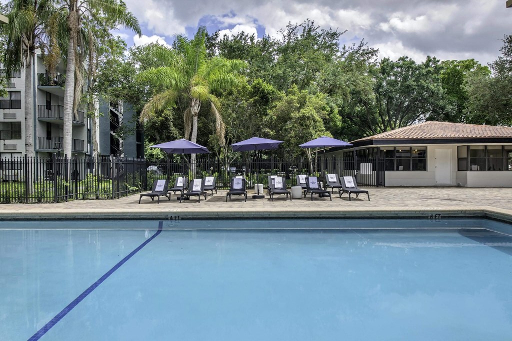 a pool with lounge chairs and umbrellas in front of a building  at Club at Emerald Waters, Hollywood, 33021