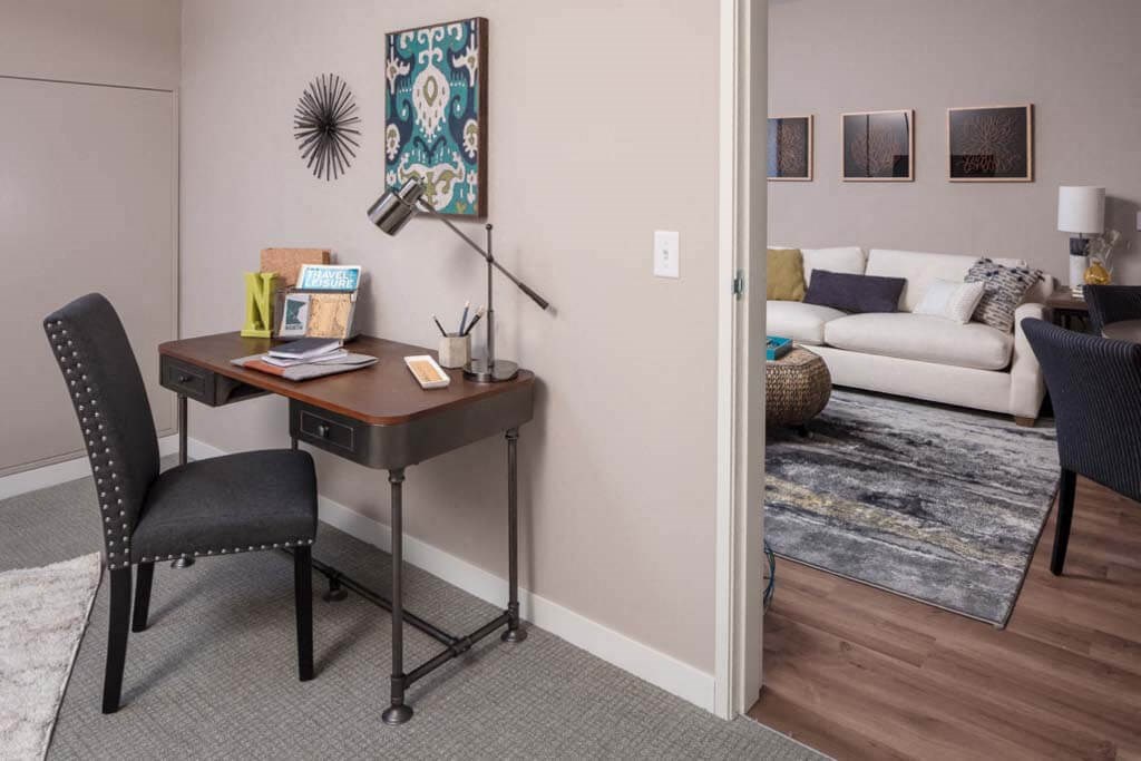 a home office with a desk and chair in front of a living room with a couch and