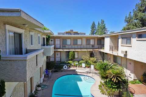 A swimming pool is surrounded by a patio with chairs and a table.
