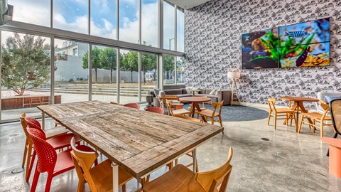 A wooden table with red chairs is in the foreground of a room with a large TV mounted on the wall.