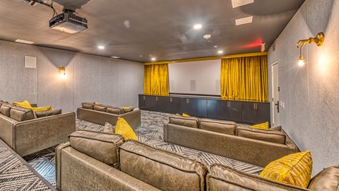 A room with a row of brown couches and a black bed with yellow curtains.
