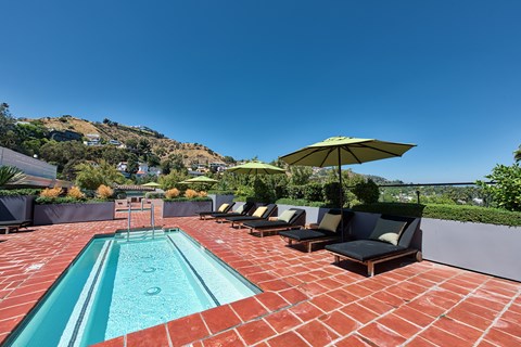 A pool with a red brick floor and a yellow umbrella.