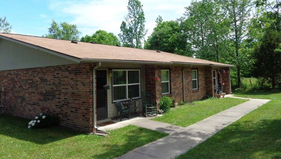 A small brick house with a porch and a green lawn.