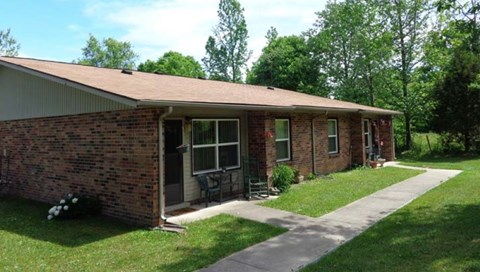 A small brick house with a porch and a green lawn.