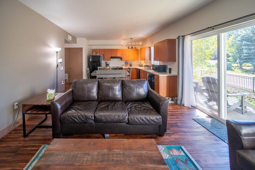 A brown leather couch sits in a living room with a kitchen in the background.