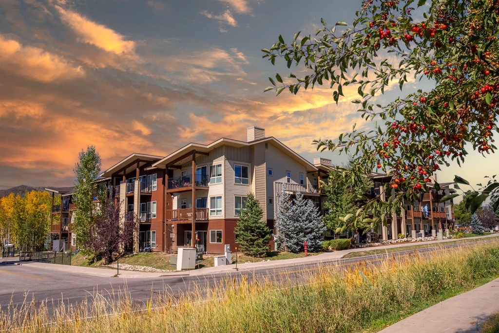 A modern apartment building with a street in front and trees around.