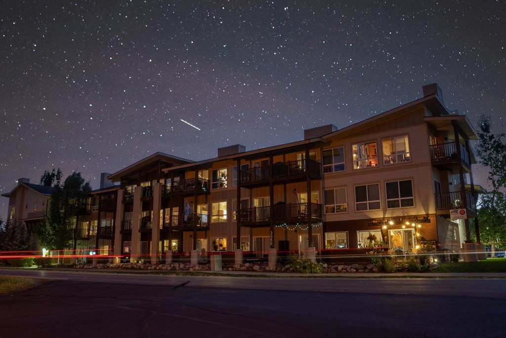 A large building with a balcony is lit up at night with a shooting star in the sky.