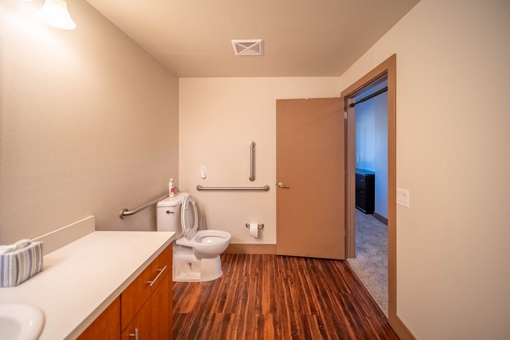 A bathroom with a toilet, sink, and wooden floors.