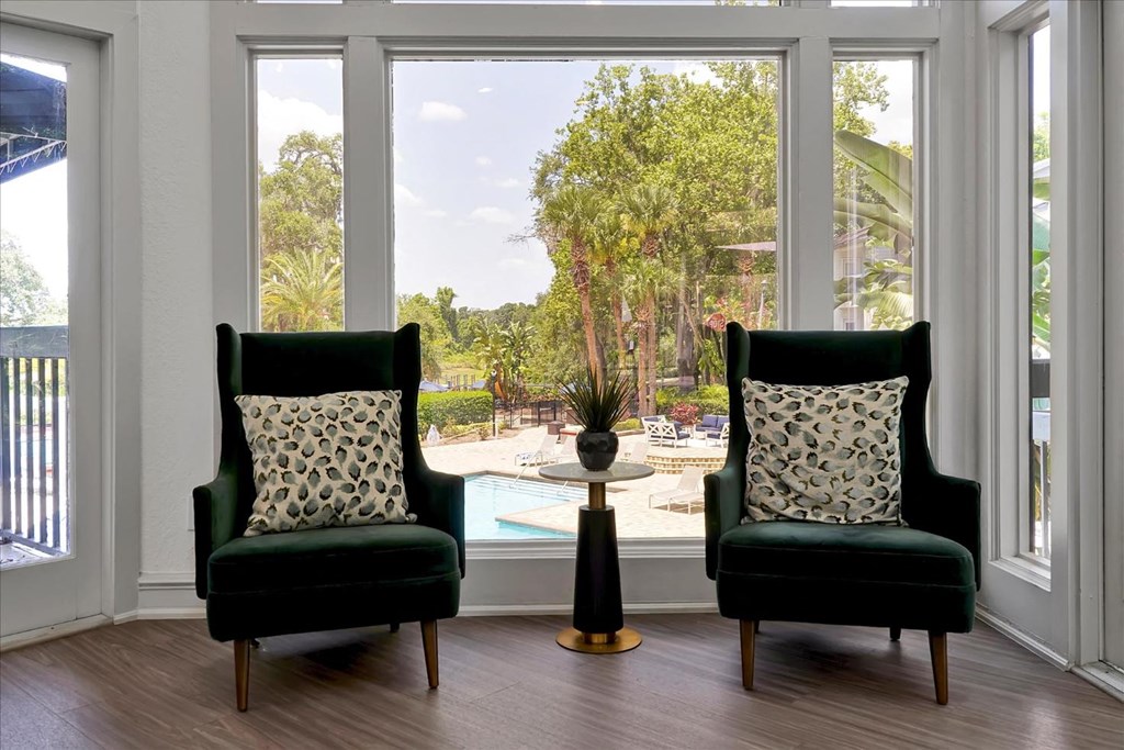 a living room with two green chairs and a view of a swimming pool
