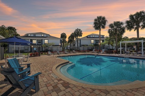 A swimming pool surrounded by a brick patio and lounge chairs.