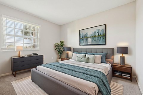 A bedroom with a large bed, a nightstand with a lamp, and a painting on the wall.