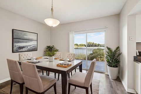 A dining room with a table set for four and a view of the outdoors through the window.
