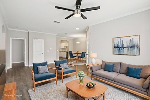 A living room with a grey couch, blue chairs, and a painting on the wall.