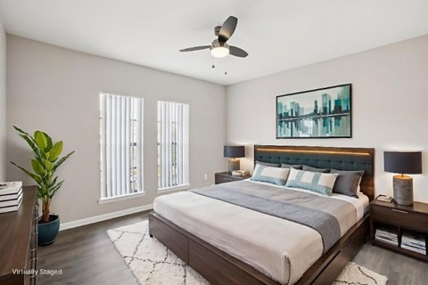 A bedroom with a large bed, a ceiling fan, and a painting on the wall.