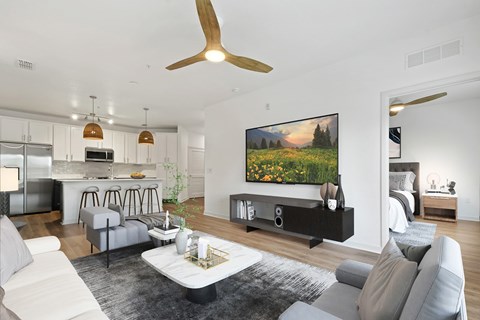A modern living room with a grey sofa set, a coffee table, a ceiling fan, and a large painting on the wall.