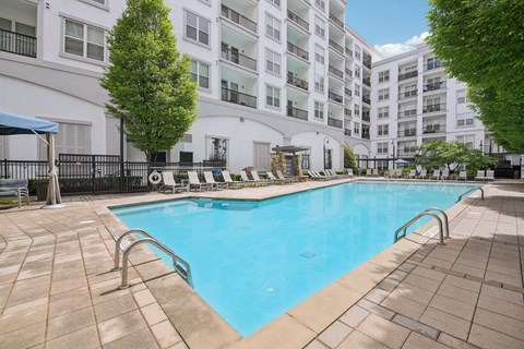 A large swimming pool surrounded by a black fence and a white building in the background.