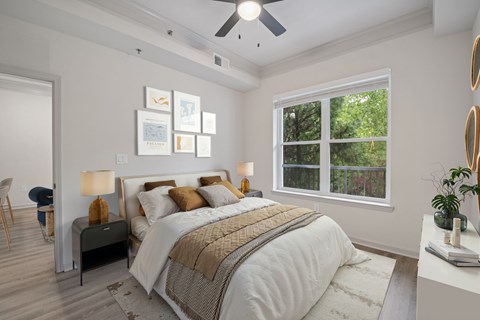 A bedroom with a large bed and a window overlooking a tree-filled yard.