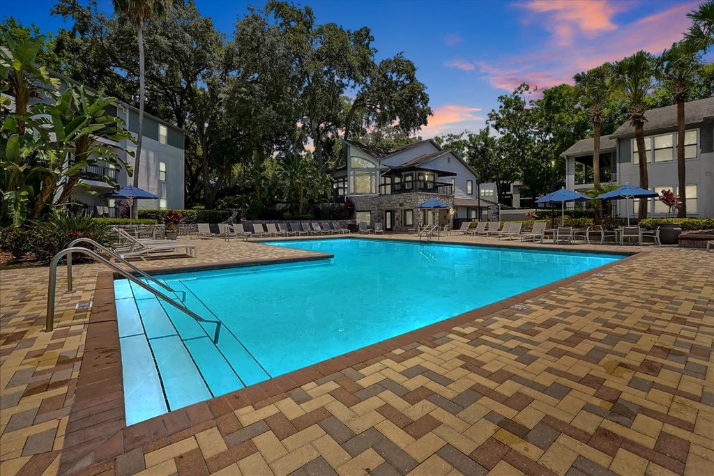 a swimming pool is surrounded by a brick patio and a building with trees