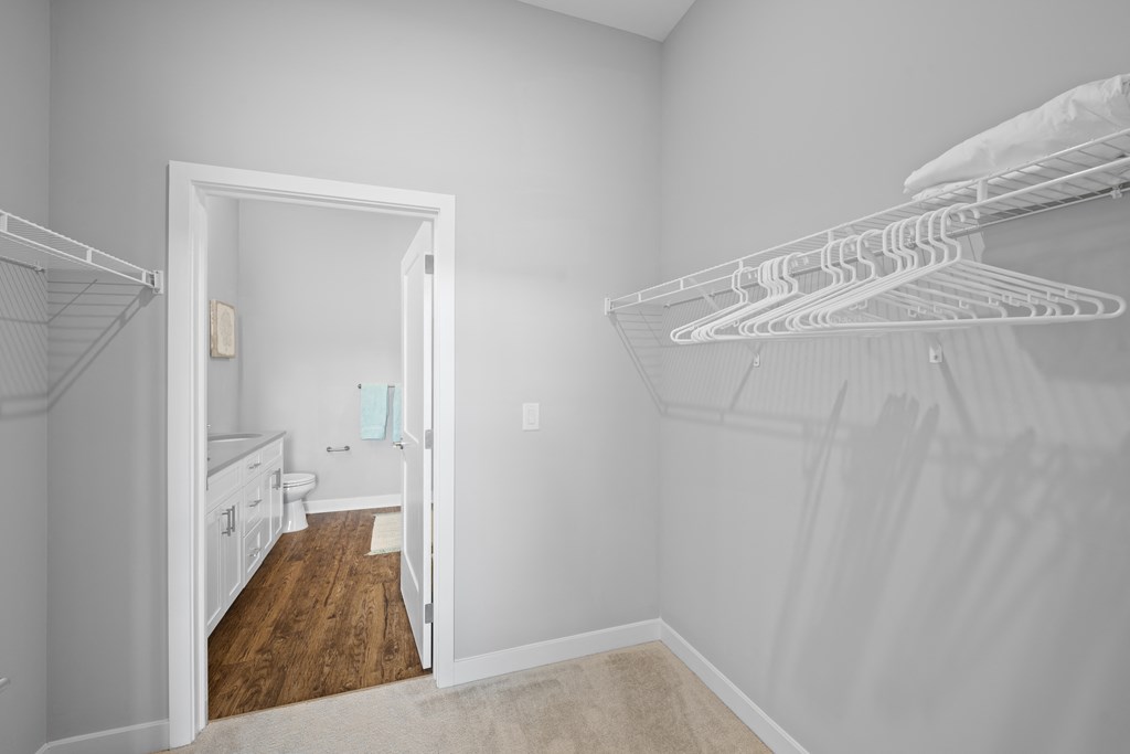 A spacious walk-in closet with clothing shelves near a doorway that leads to a private bathroom.