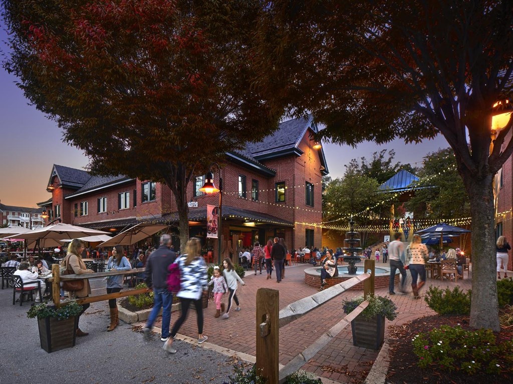 A group of people are walking through a plaza with a tree with red leaves.