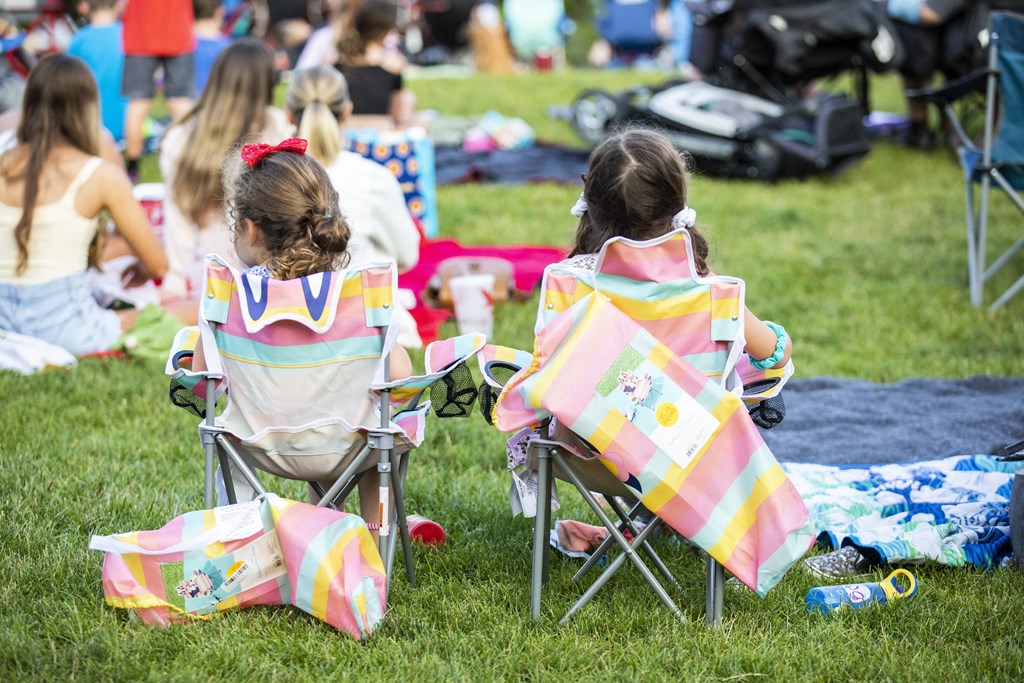 Two girls sitting in chairs with colorful blankets on the grass.