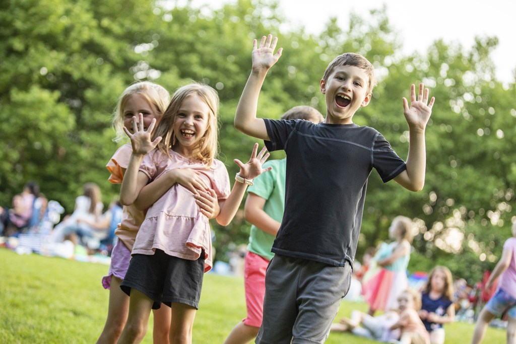 Three children are playing in a park with their hands up in the air.
