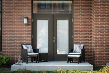 two chairs on a porch in front of a brick building