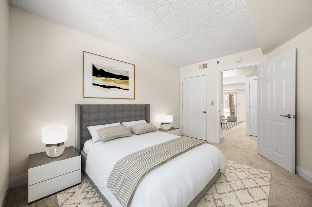 A bedroom with a large bed, a nightstand with a lamp, and a painting on the wall.