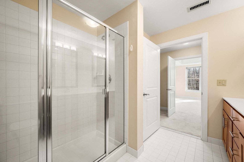 A bathroom with a glass shower door and a white tiled floor.