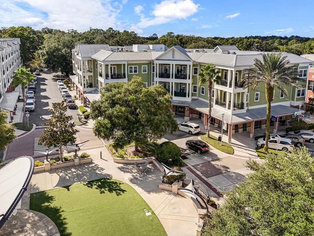 A sunny day at a residential complex with cars parked and trees surrounding the buildings.