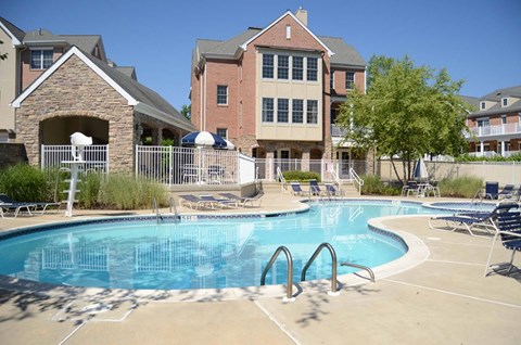 A swimming pool surrounded by chairs and umbrellas in front of a building.