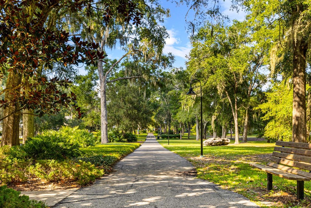 A park with a walking path, trees, and a bench.
