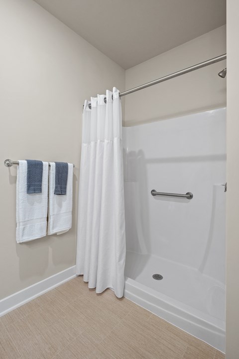 a bathroom with a shower with a white shower curtain and towels