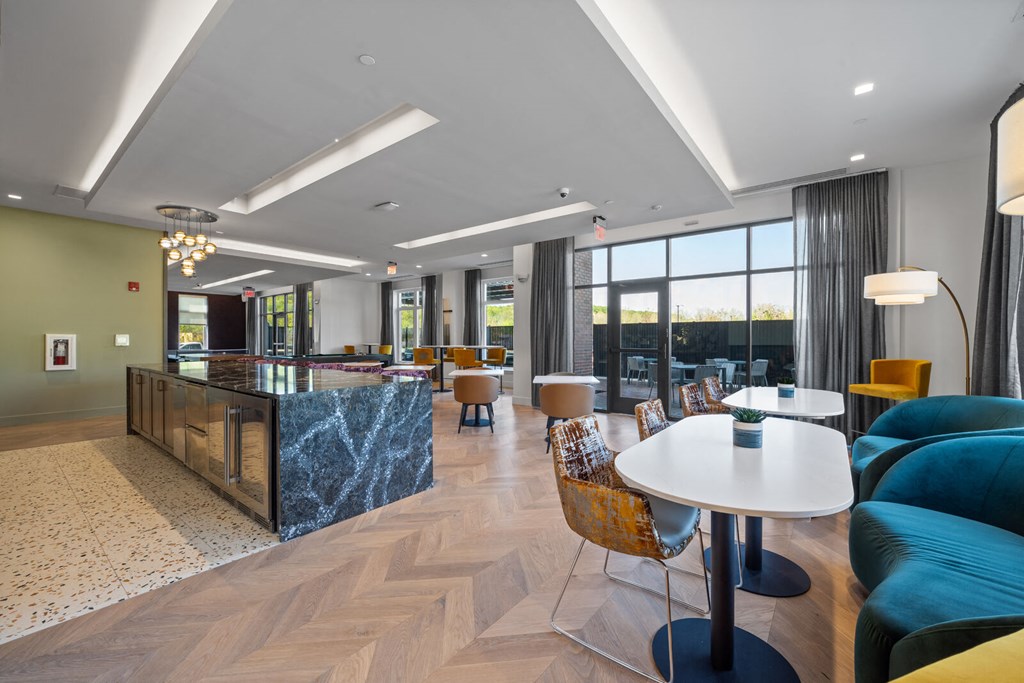 A community kitchen and resident lounge with a long bar, tables, chairs, and large windows.