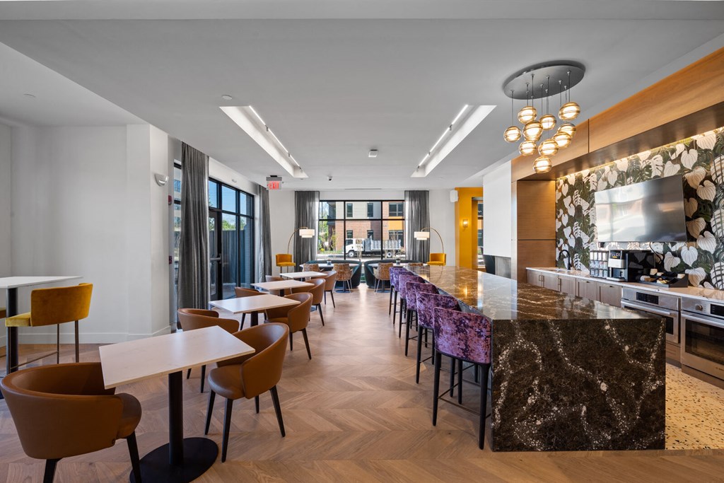 A long bar with modern purple barstools, tables and chairs, and a TV in a resident lounge with a community kitchen.