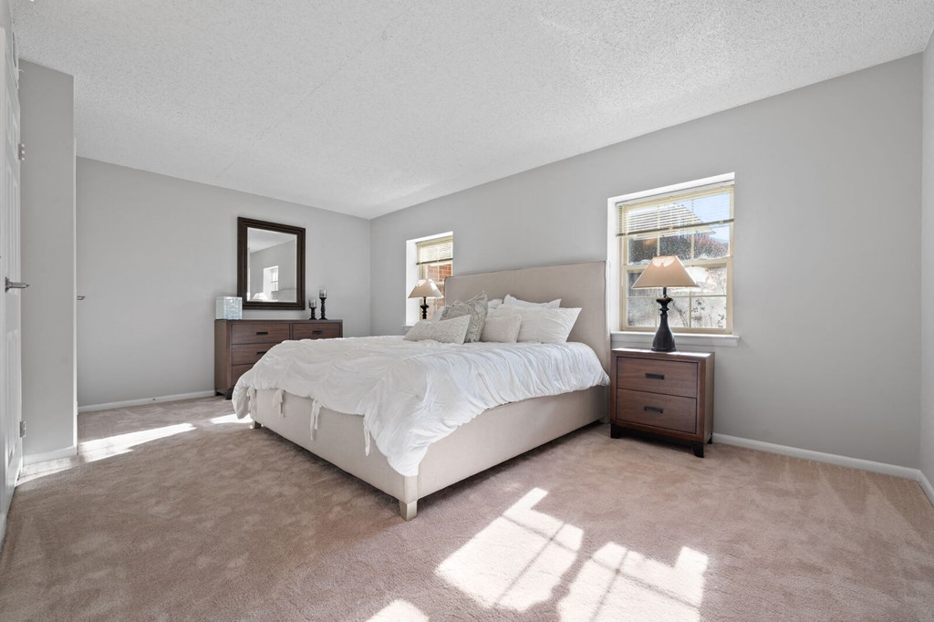A large bedroom with two windows, ample natural light, carpet flooring, and access to the hallway.