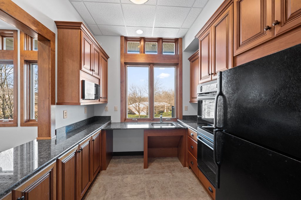 A community kitchen in the clubhouse at New Kent Apartments in West Chester, PA, featuring a large window, black appliances, a sink, and granite countertops