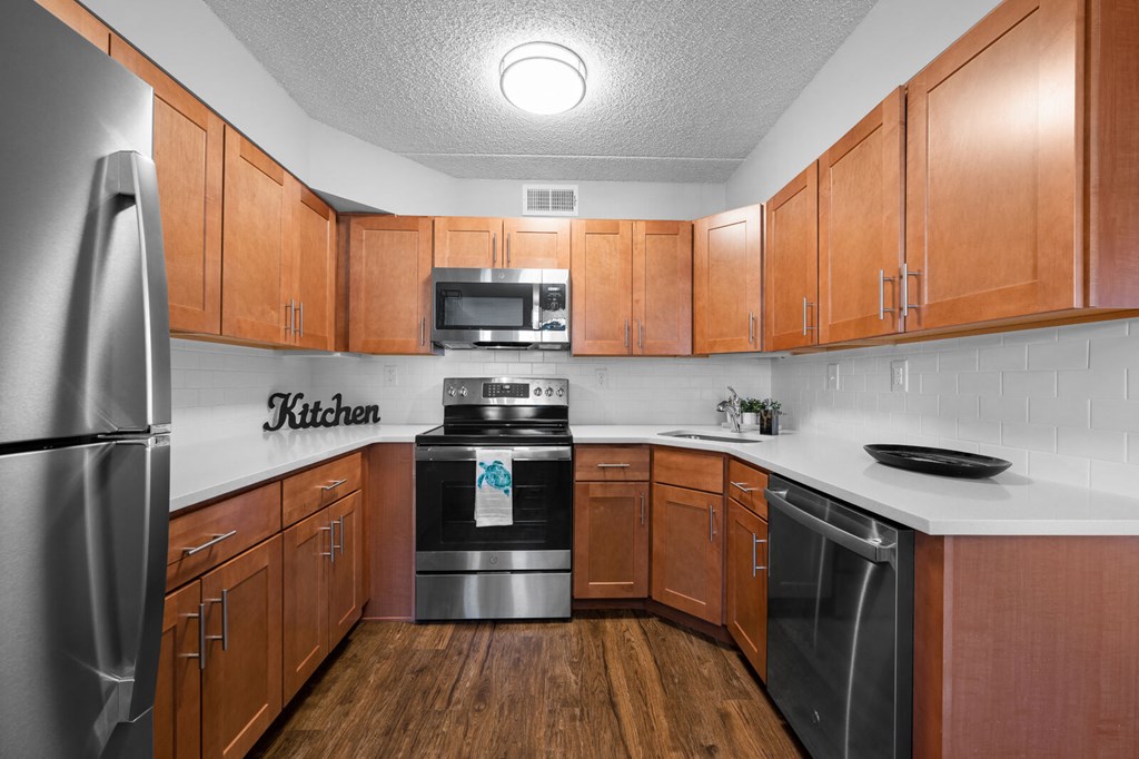 Stylish U-shaped kitchen with stainless steel appliances, a sleek subway tile backsplash, durable quartz countertops, and elegant hardwood-style flooring at New Kent Apartments, West Chester, PA
