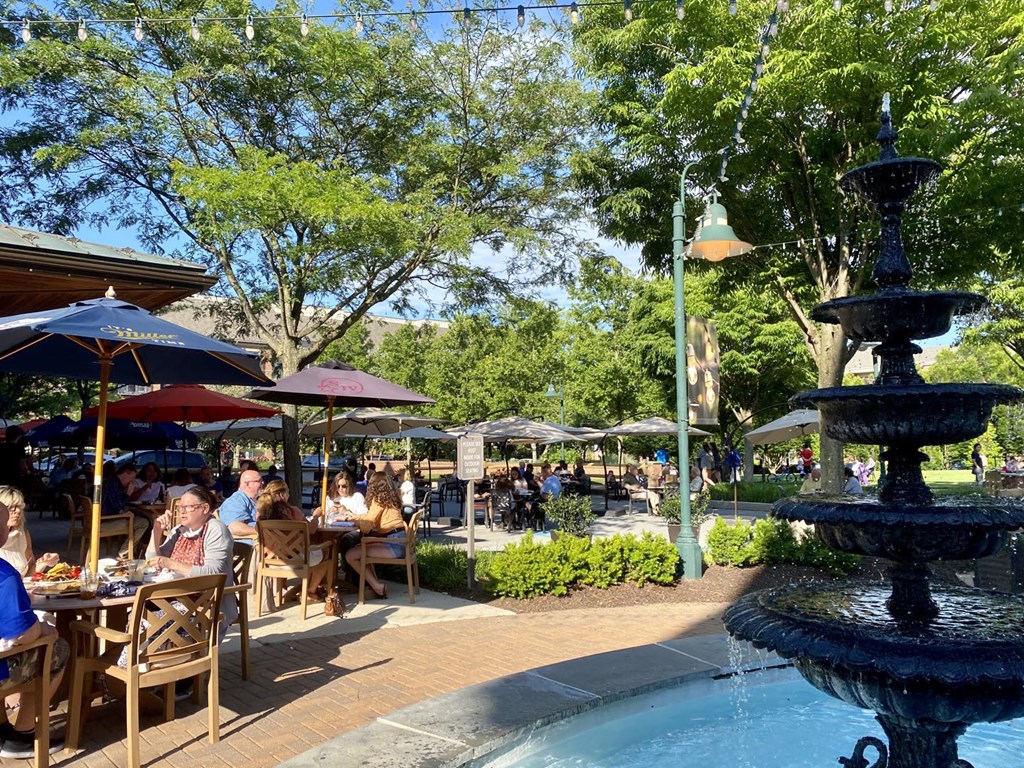 A fountain in the middle of a plaza with people sitting at tables.