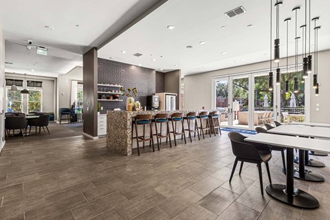 Community lounge with granite island, bar seating, tables, and patio doors at The Flats at Tioga Town Center.