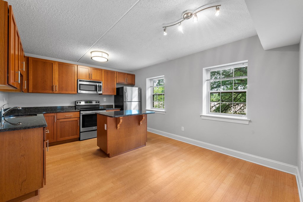 Bright and spacious kitchen featuring stainless steel appliances, a central kitchen island, two windows for natural light, and hardwood-style flooring at New Kent Apartments, West Chester, PA