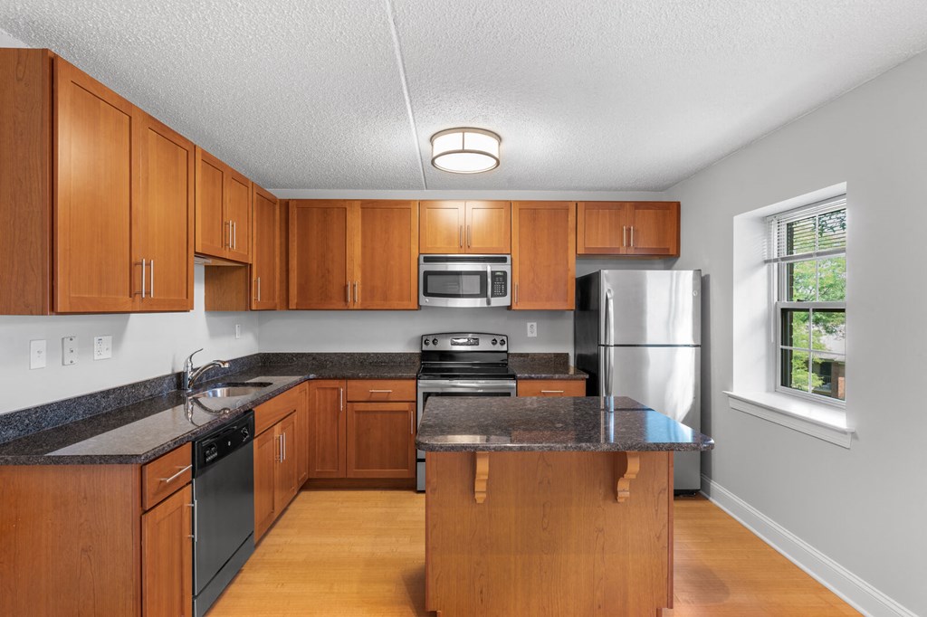 An L-shaped kitchen with a window, granite countertops, stainless steel appliances, and hardwood-style flooring.