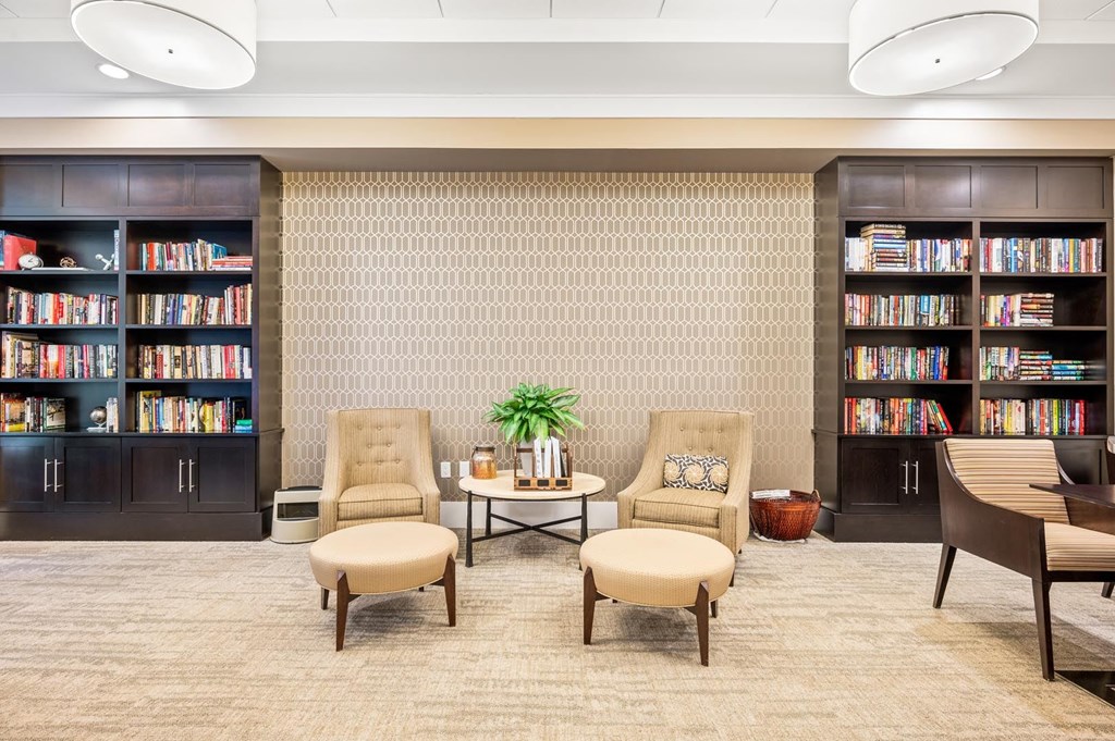 A room with a carpeted floor, two chairs, a table, and bookshelves filled with books.