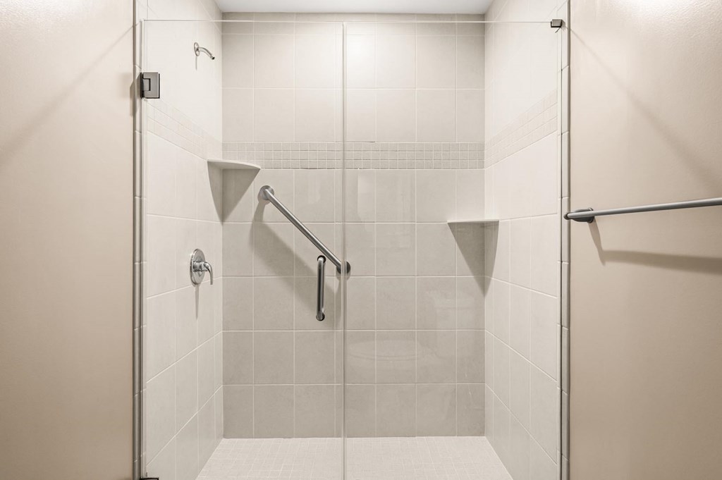 A white tiled shower with a glass door and a metal grab bar.