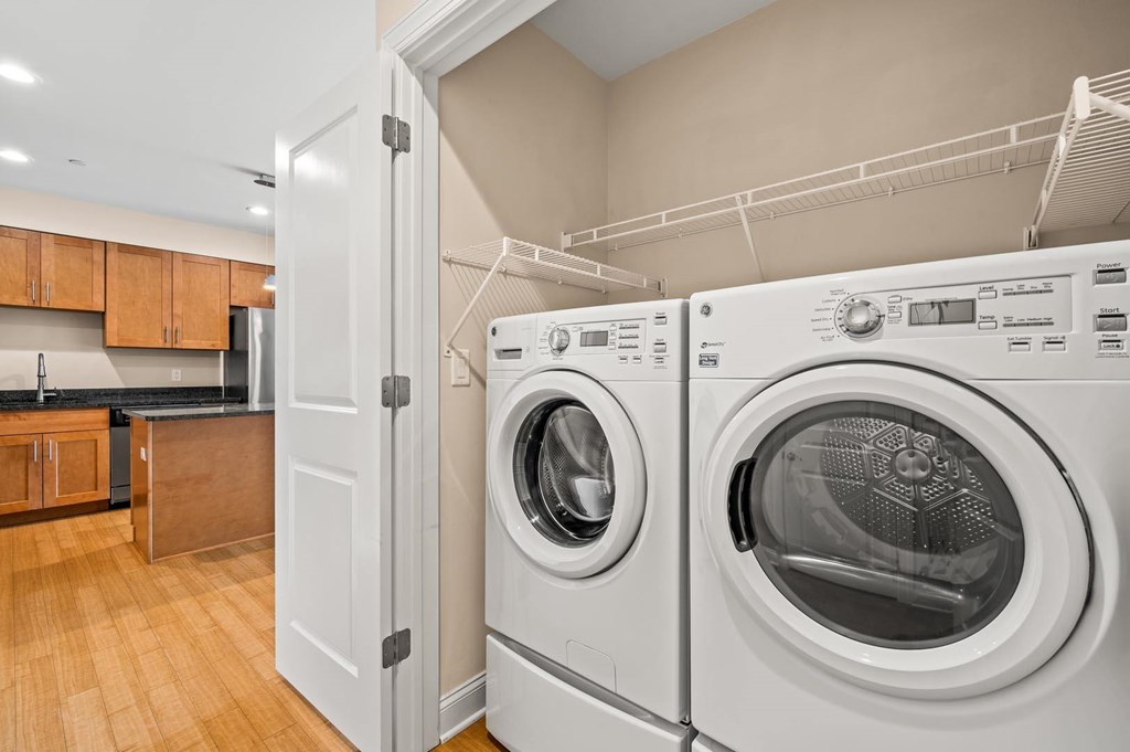 A white door is open to reveal a laundry room with a washer and dryer.