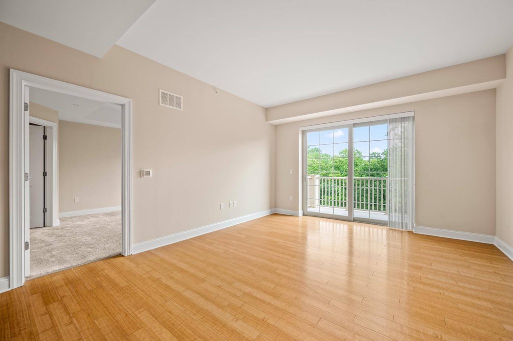 A room with wooden floors and a sliding glass door leading to a balcony.