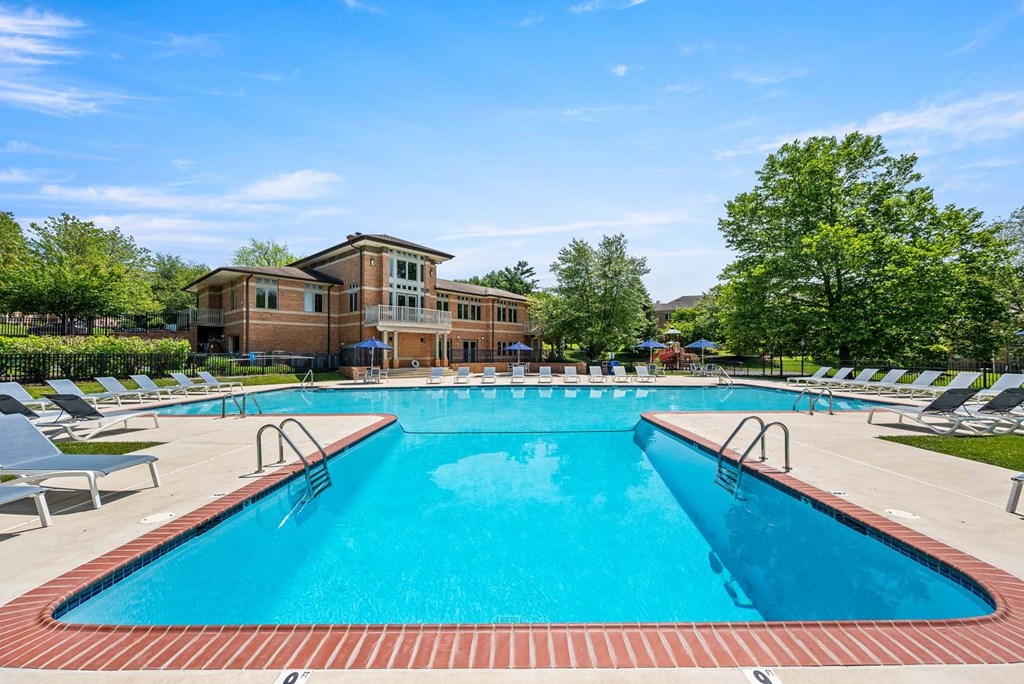 A large swimming pool with a red brick border and a building in the background.