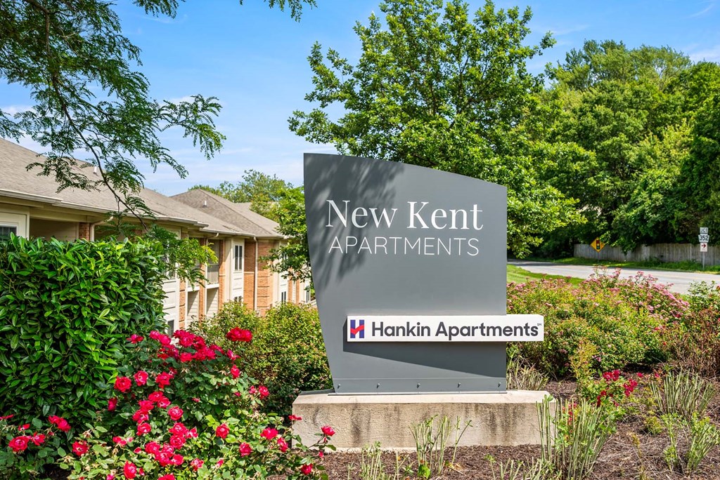 A sign for New Kent Apartments by Hankin Apartments stands in front of a building.